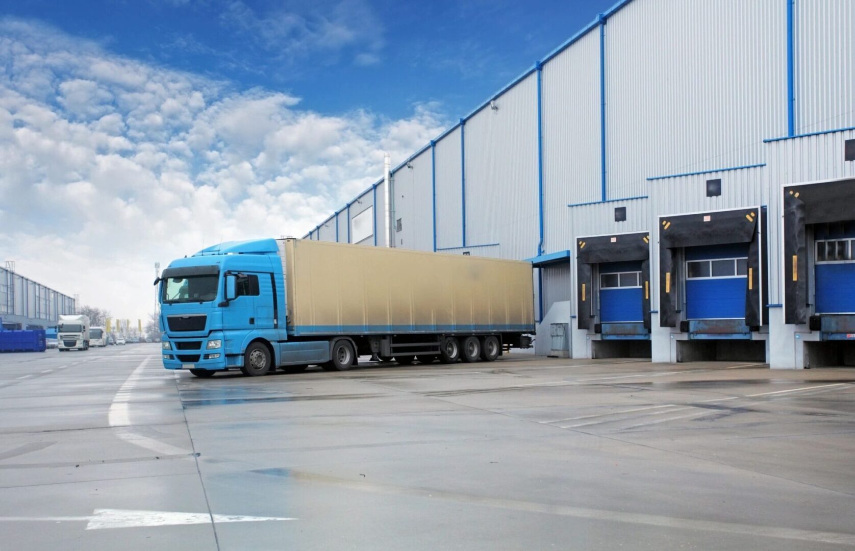 A blue truck parked at a loading dock outside a warehouse.