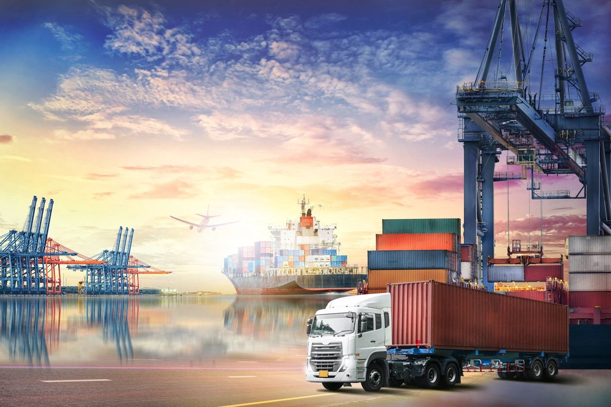 Cargo truck unloading containers at a busy port during sunset.