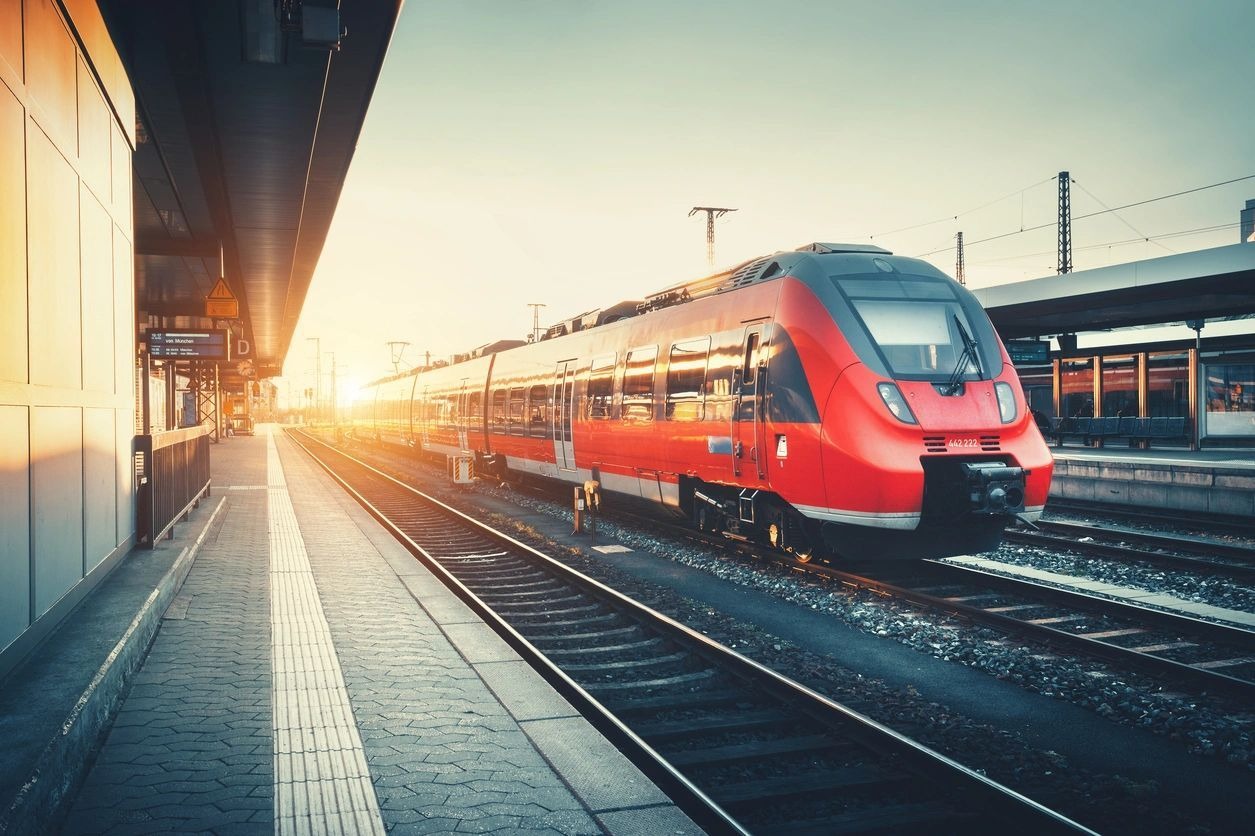 Modern red train at station during sunset.